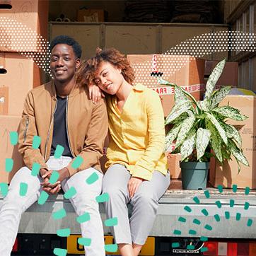 Couple sitting on the back of a moving truck with boxes behind them